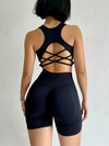 Person wearing a black strappy top and high-waisted shorts on a plain background