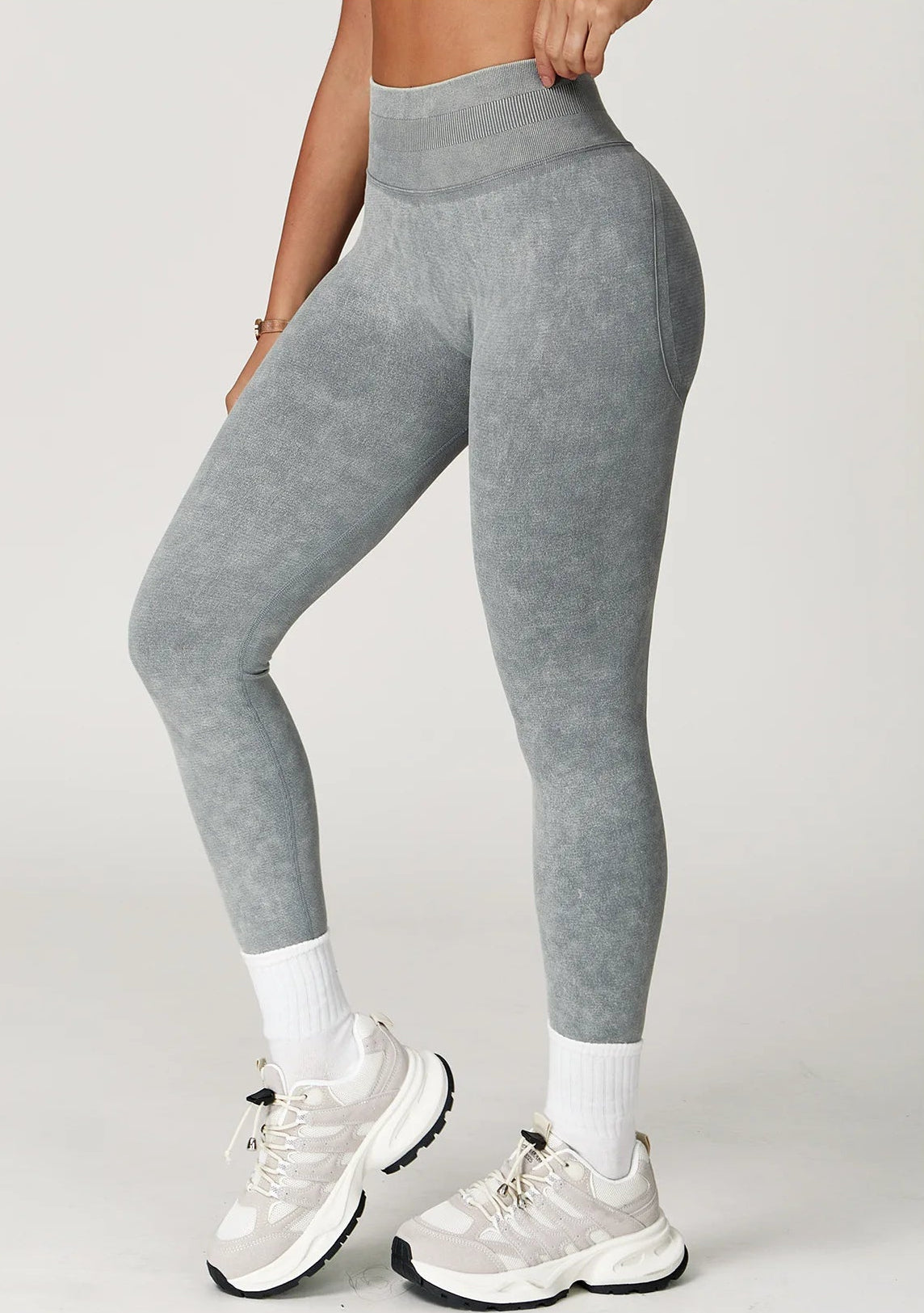 Person wearing gray high-waisted leggings with white sneakers on a light gray background