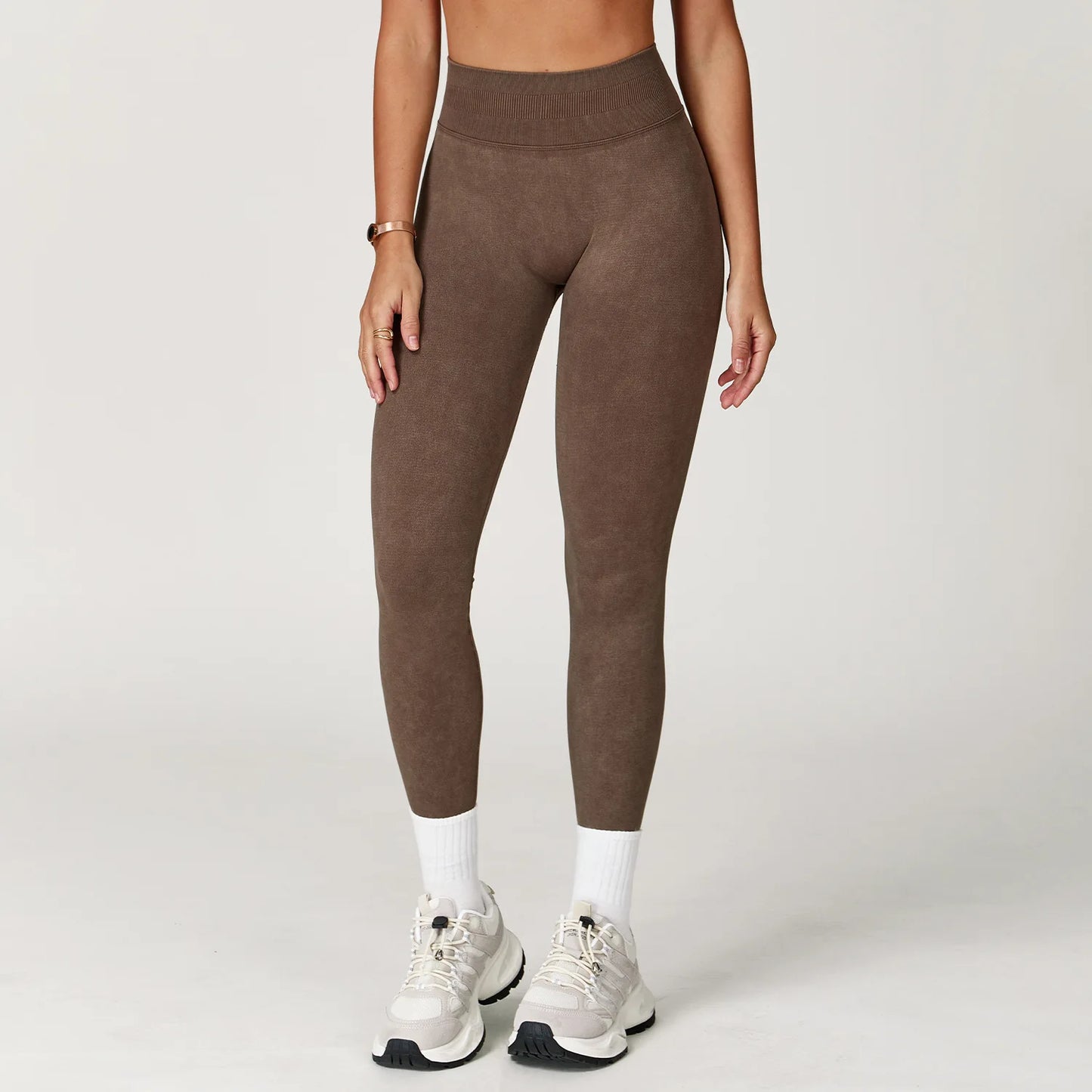 Person wearing brown leggings and white sneakers on a plain background